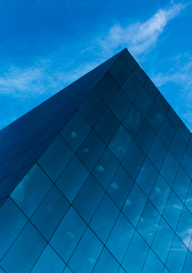 Modern blue glass building reflecting a clear sky and clouds, Carl Willis leadership and business insights.
